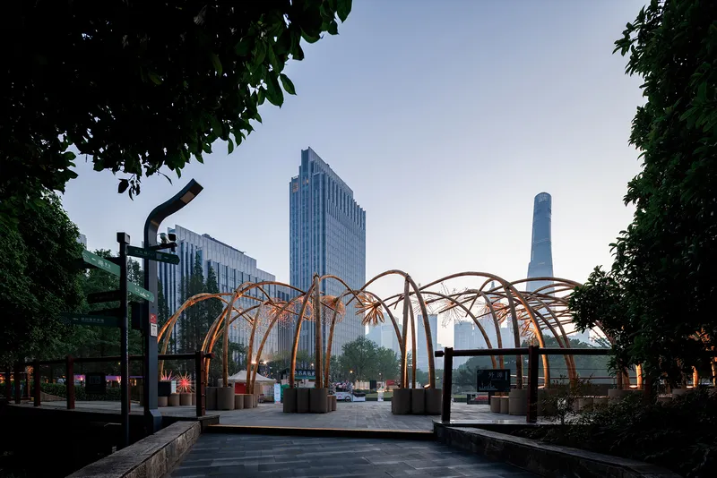 Illuminated bamboo canopy in a public plaza with highrise towers visible in the evening haze