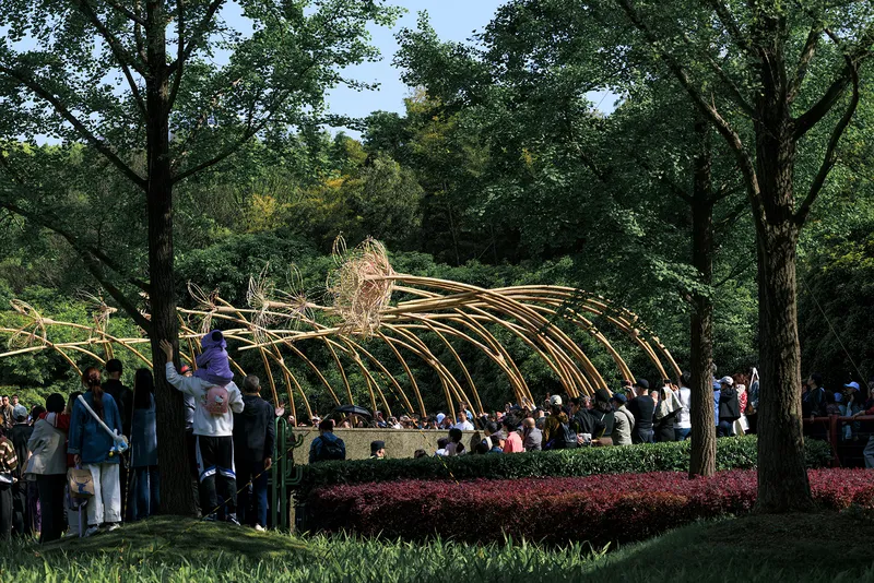 Visitors gathering around the bamboo pavilion among mature trees and flowering shrub borders in daylight