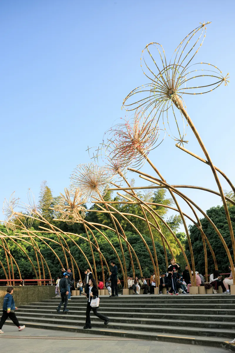 Woven bamboo flower sculptures on slender stems rising above the arched canopy against a clear sky