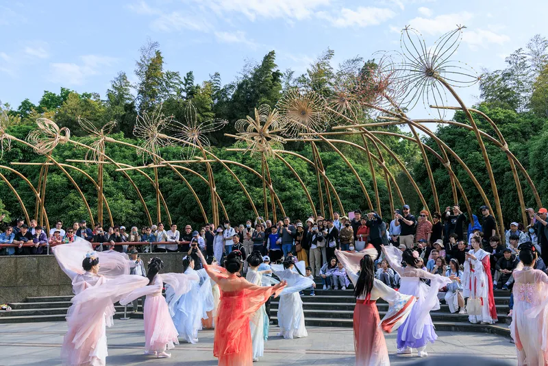 Performers in flowing costumes dancing on the plaza beneath the bamboo arches with spectators on the steps