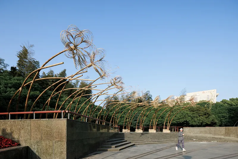 Arching bamboo structures with wirework canopies along terraced plaza as visitor crosses the space