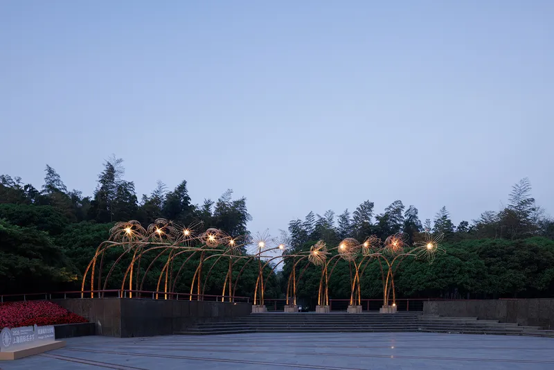 Wide view of the arching canopy installation spanning a terraced concrete plaza under an overcast sky