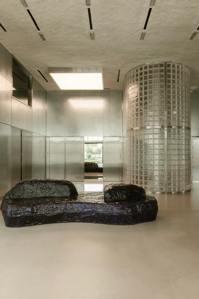 Black volcanic stone bench beside a cylindrical glass block column under a skylight