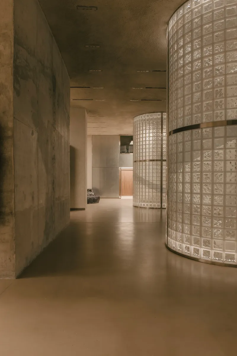 Corridor with curved glass block wall and cast concrete surfaces under ambient light