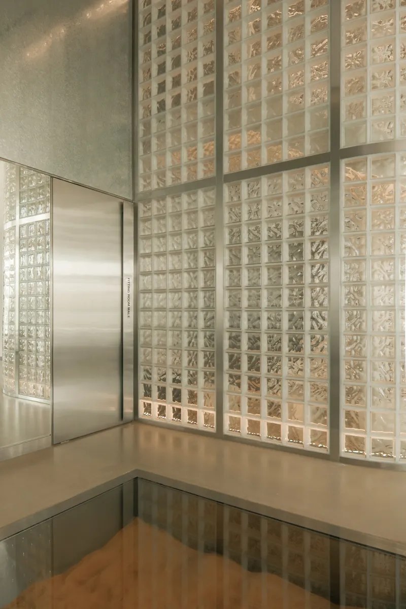 Corner detail of glass block wall and stainless steel door frame reflected in polished floor