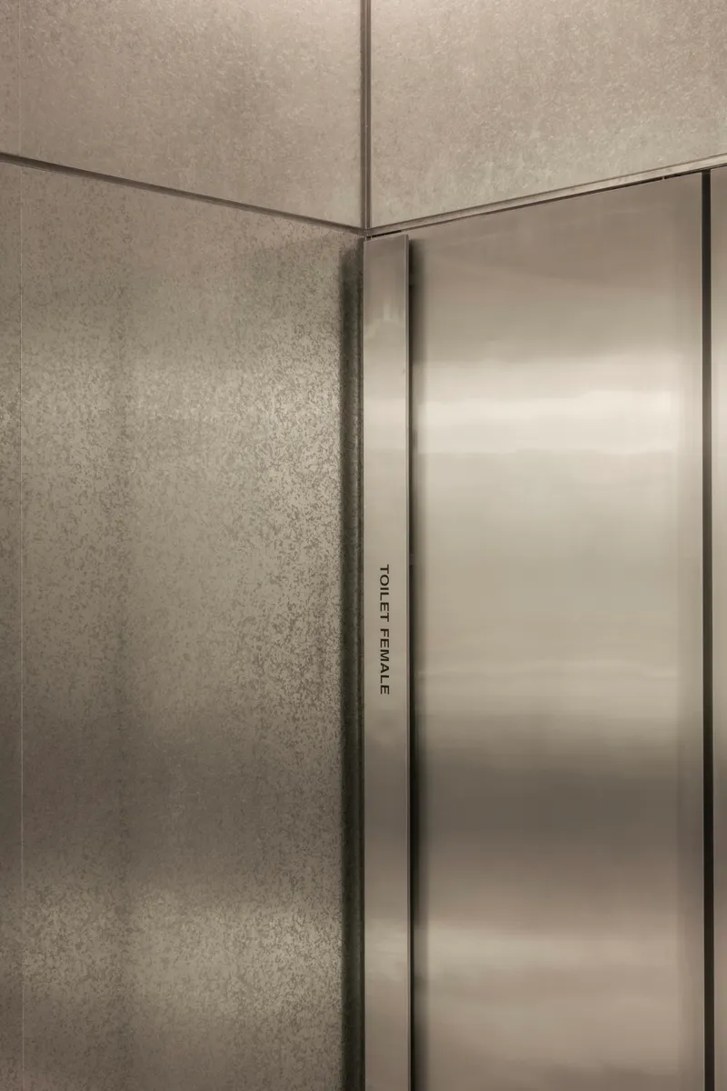 Close-up of brushed stainless steel door edge against textured concrete wall corner