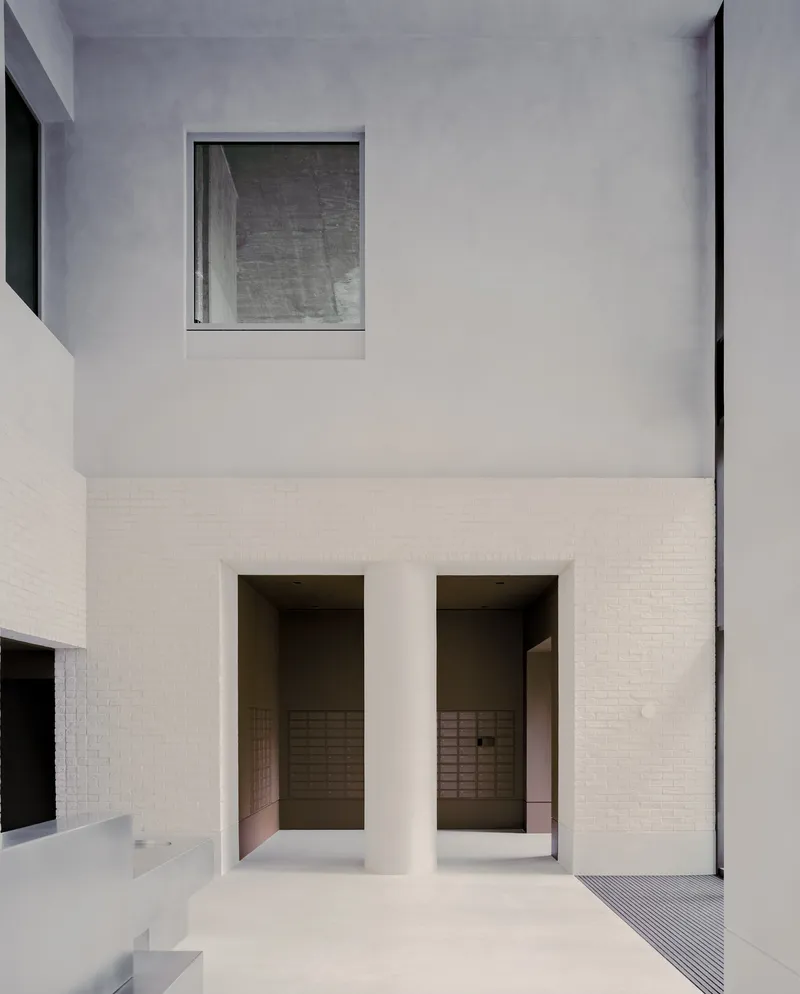 Courtyard view showing two deep-set openings in a white brick base beneath rendered upper walls