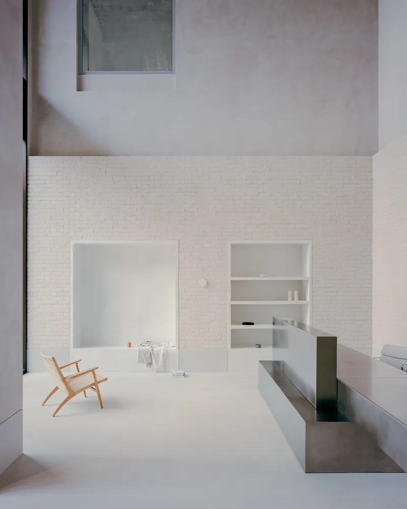 Double-height courtyard with white brick walls and a timber chair on pale flooring