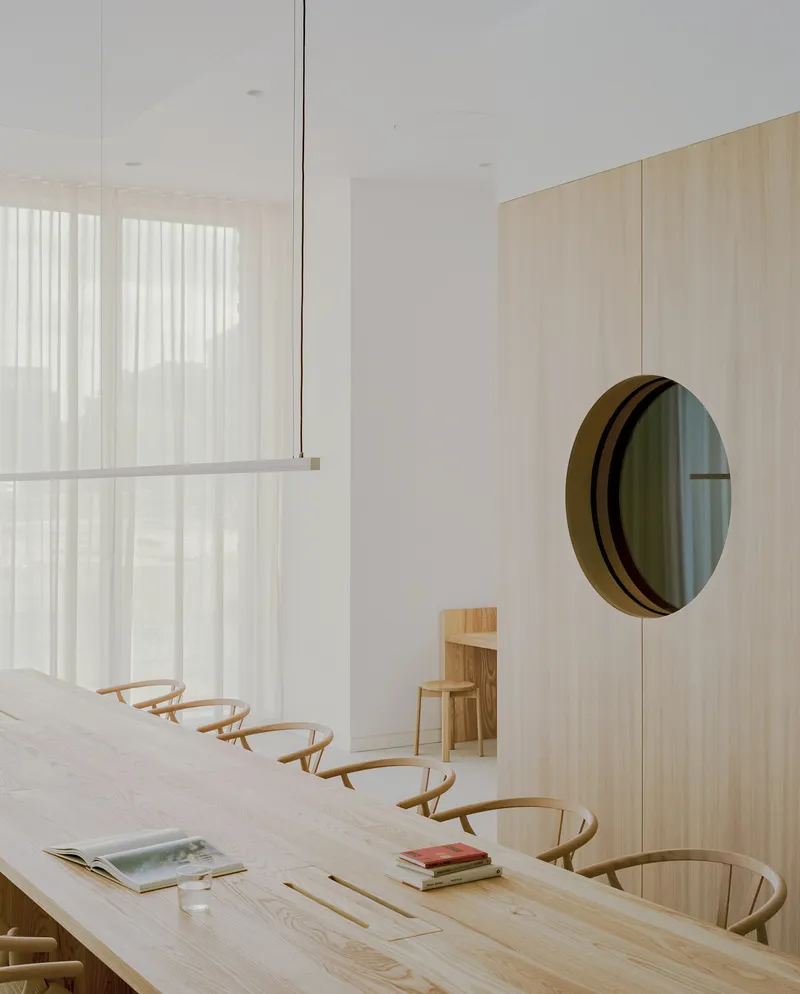 Timber dining table with curved-back chairs and circular mirror mounted on pale veneer wall