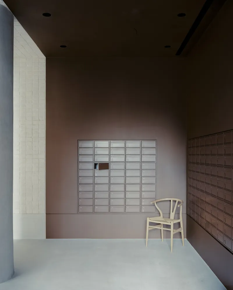 Entry vestibule with grid of frosted glass letterboxes set into terracotta-colored plaster wall