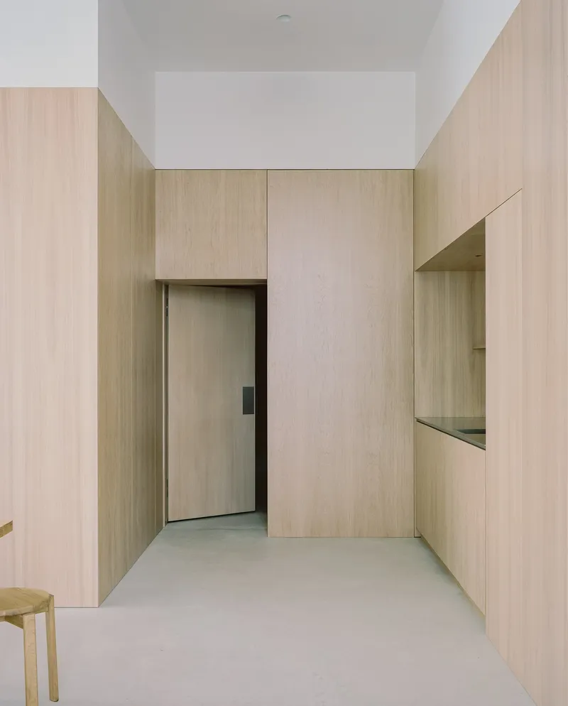 Light timber-paneled corridor with recessed door and built-in display niche under white ceiling with clerestory