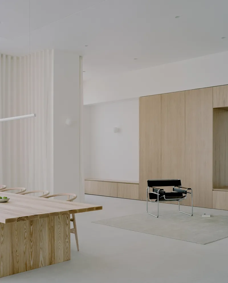 Open living space with timber dining table and built-in cabinetry beneath white ceiling and sheer curtains