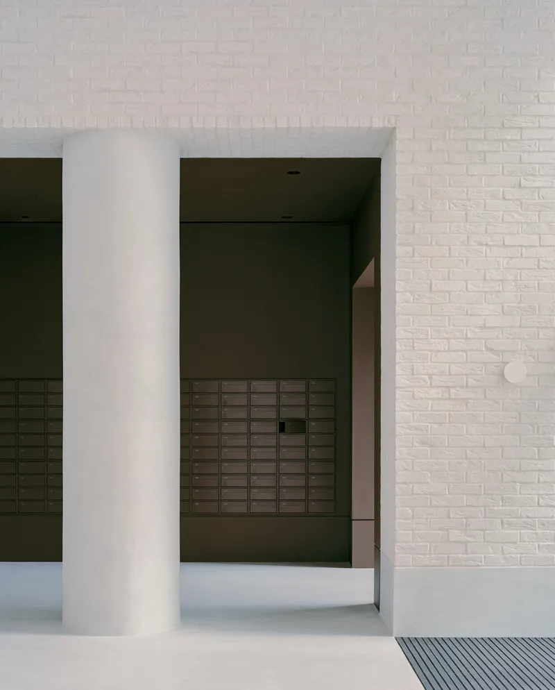 Covered entrance with white circular column framing a view into a dark vestibule with mailboxes