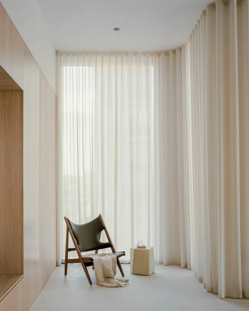 Curved alcove with floor-to-ceiling sheer curtains filtering daylight beside a walnut lounge chair