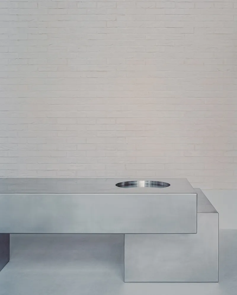 Cantilevered stainless steel countertop with circular basin against white painted brick wall