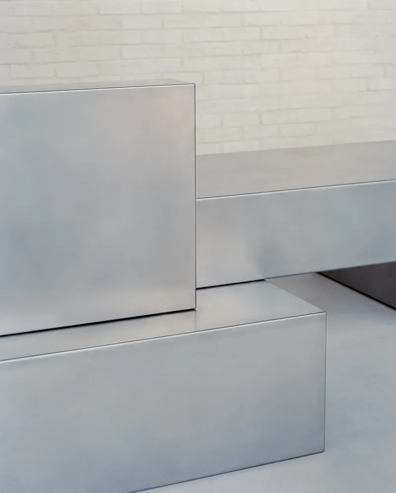Detail of stainless steel counter edges and joints meeting white brick wall and grey flooring
