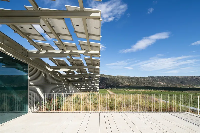 Timber pergola shading a white deck terrace overlooking cultivated fields under blue sky