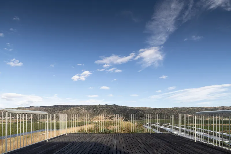 Timber deck terrace with metal railing facing distant hills under afternoon sky