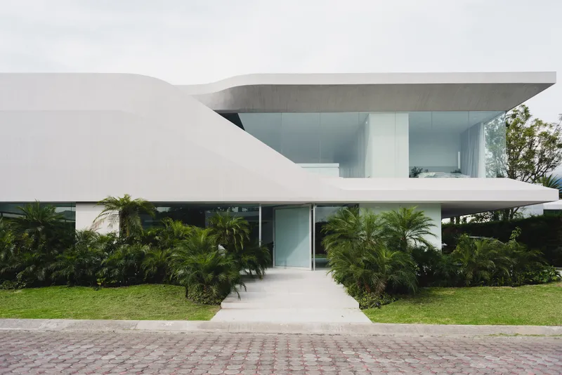 Street view of the white horizontal volumes with cantilevered upper floor and palm plantings in the lawn