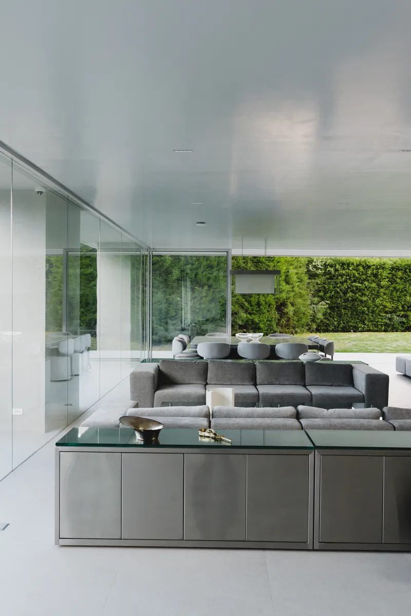 Open plan living area with floor-to-ceiling glass walls overlooking the lawn and garden hedge