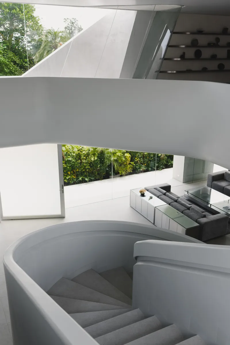 Curved concrete staircase descending beneath a sculptural white overhang with trees visible beyond