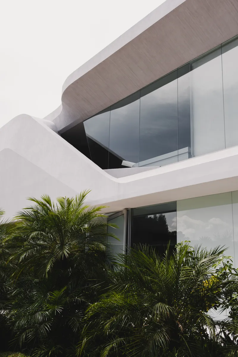 Exterior facade detail showing the curved upper balcony soffit with palms in the foreground
