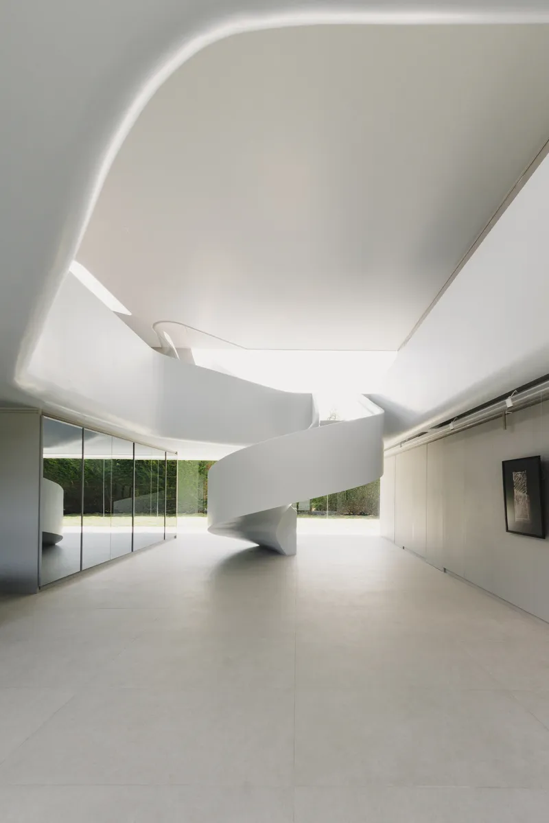 Curved white spiral staircase beneath a sculpted ceiling with concealed perimeter lighting