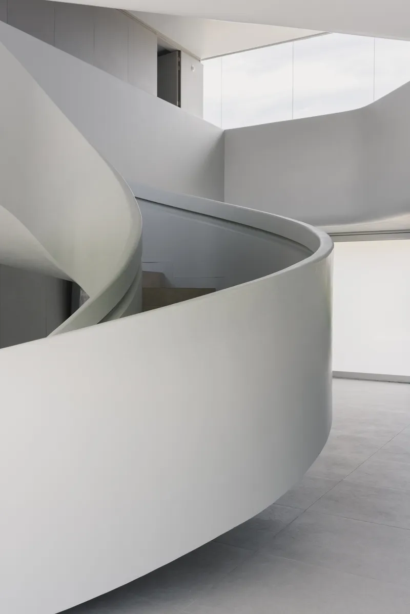 Spiraling white staircase with smooth curved walls rising through a light-filled interior space