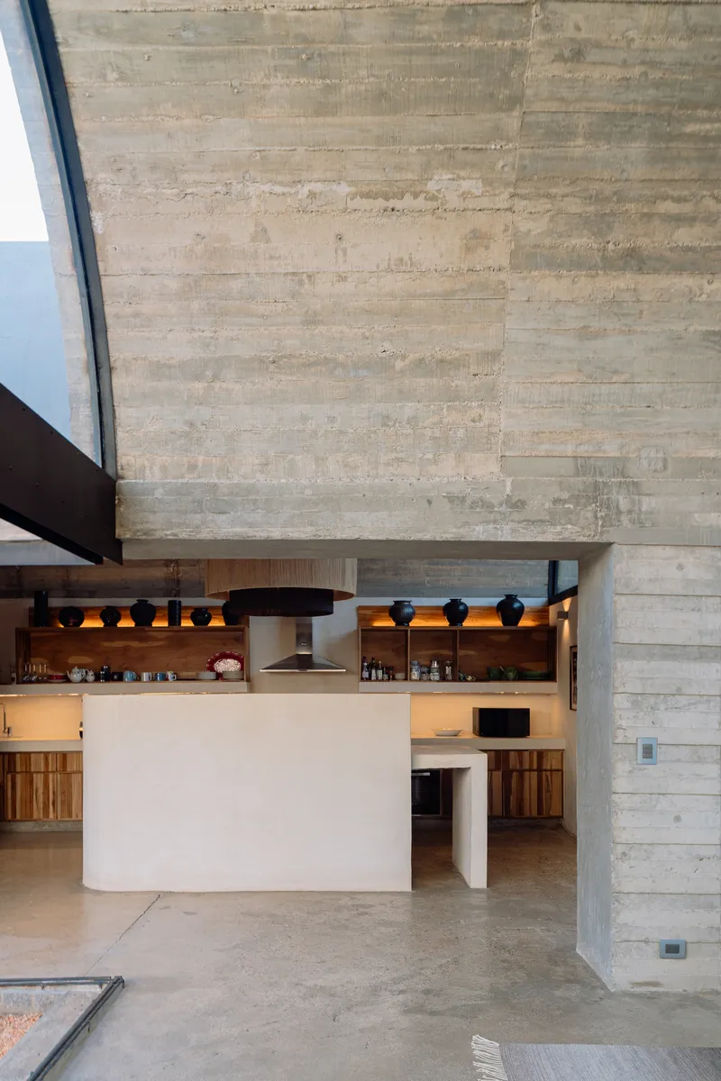 Board-formed concrete wall rising above a white plaster kitchen island with timber cabinets