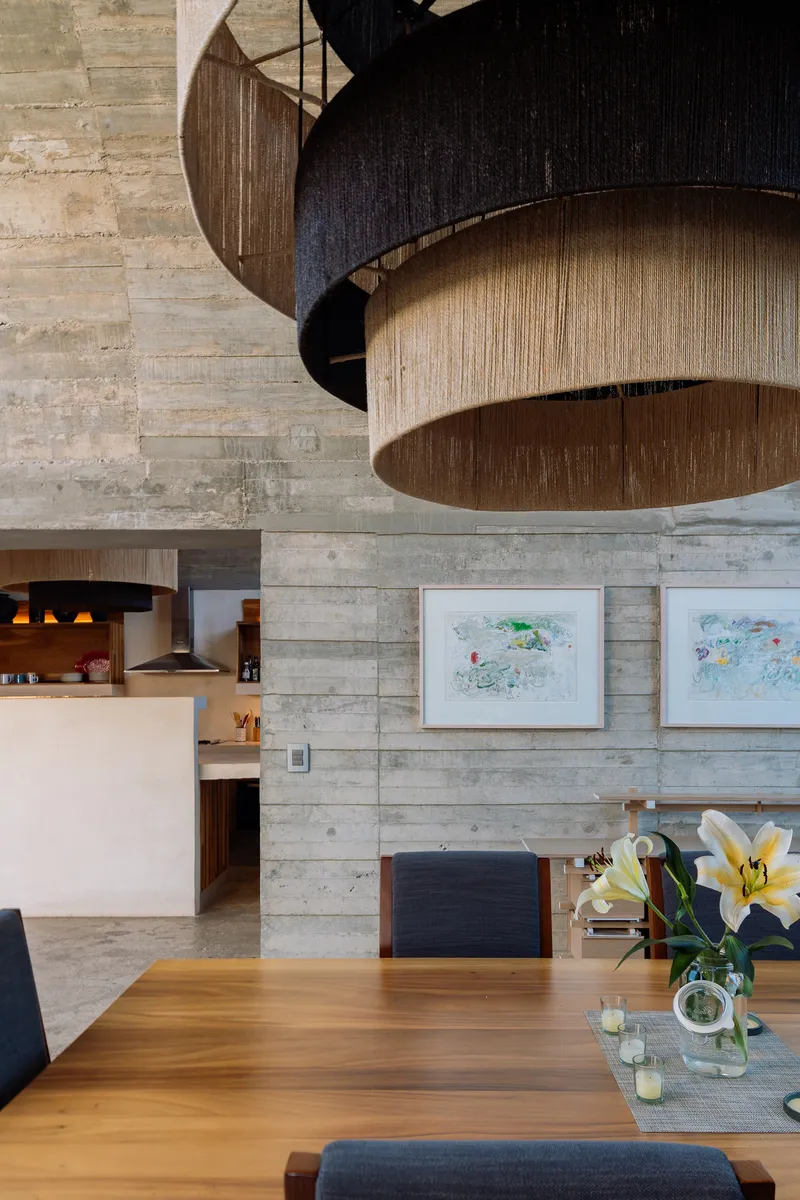 Layered timber pendant lights suspended from a board-formed concrete ceiling above the dining table