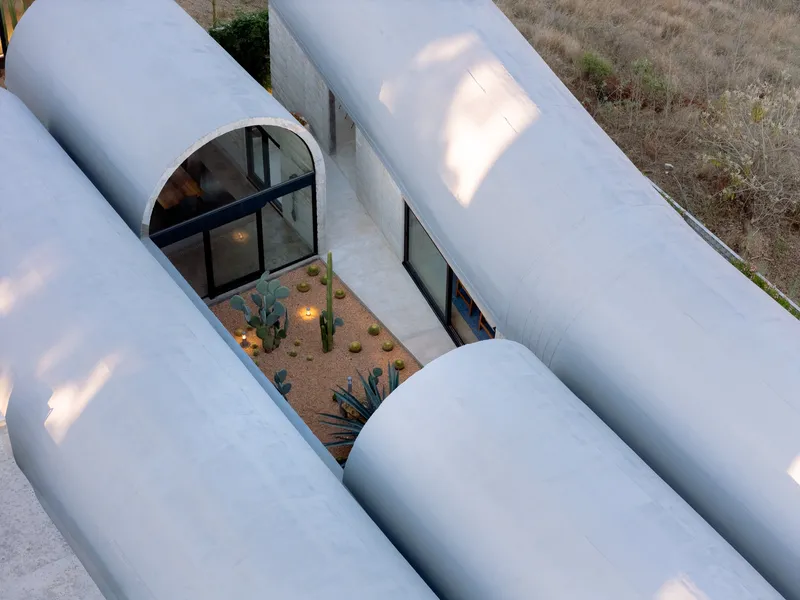 Aerial view between white barrel vaults revealing courtyard with cacti and ground lighting at dusk