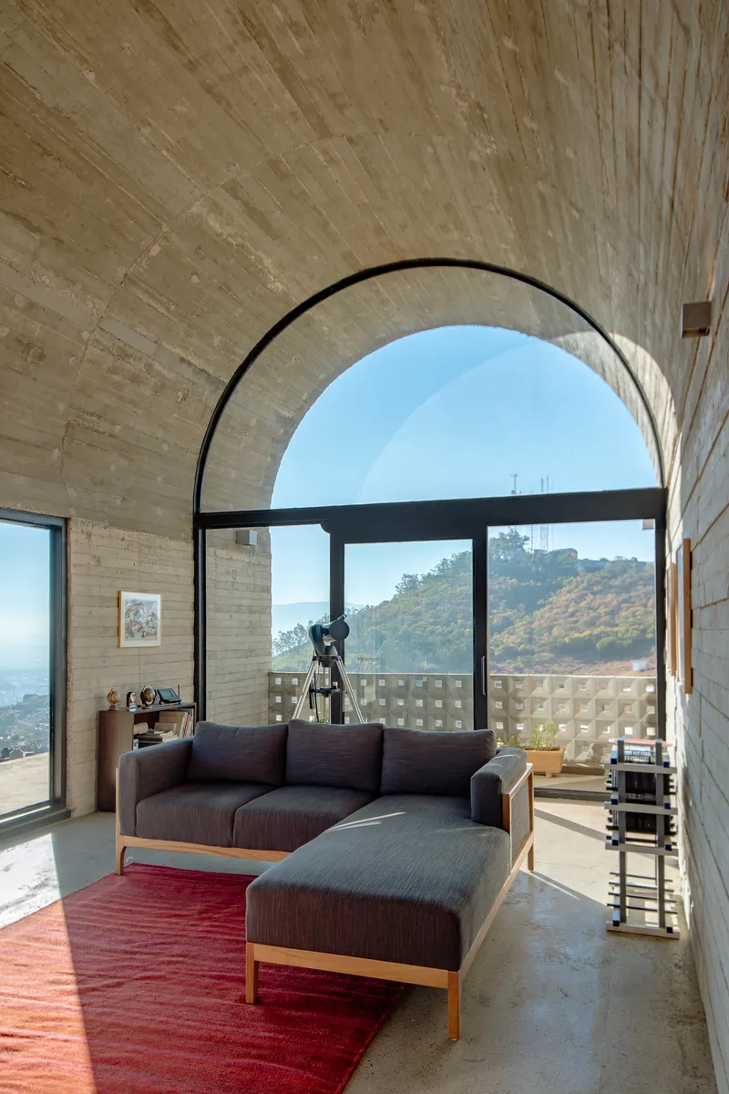 Seating area beneath a board-formed concrete arch with hillside views through the black-framed glazing