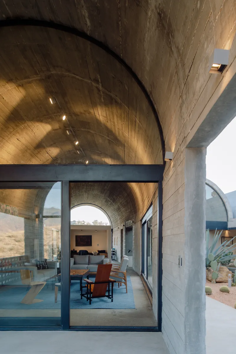 Barrel-vaulted board-formed concrete ceiling over an open living space with full-height glass walls and desert landscape beyond