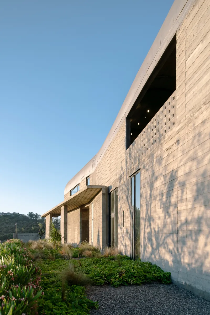 Board-formed concrete facade with perforated screen and cantilevered canopy casting shadows in afternoon light