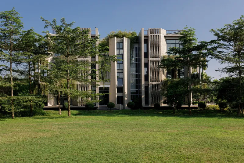 Garden elevation showing perforated concrete screens and glass facades framed by mature trees under clear sky