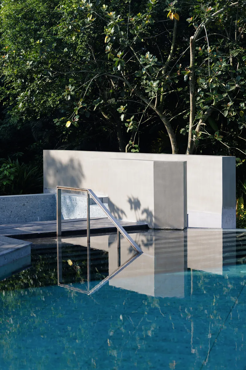 Swimming pool with stainless steel ladder and white plaster wall reflecting in still water