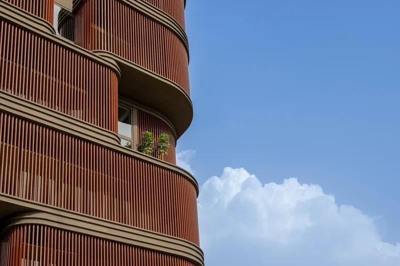 Curved timber facade with recessed balconies beneath white cumulus clouds