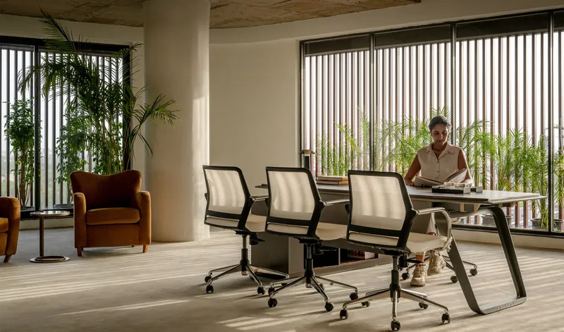 Office interior with exposed concrete ceiling, vertical louvers, potted palms and a person at desk