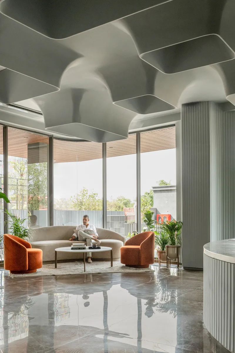 Lobby interior with sculpted white ceiling coffers, polished stone floor, fluted columns and orange lounge chairs