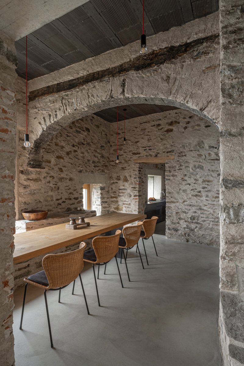 Dining room with exposed stone masonry arch and long timber table beneath a corrugated metal ceiling