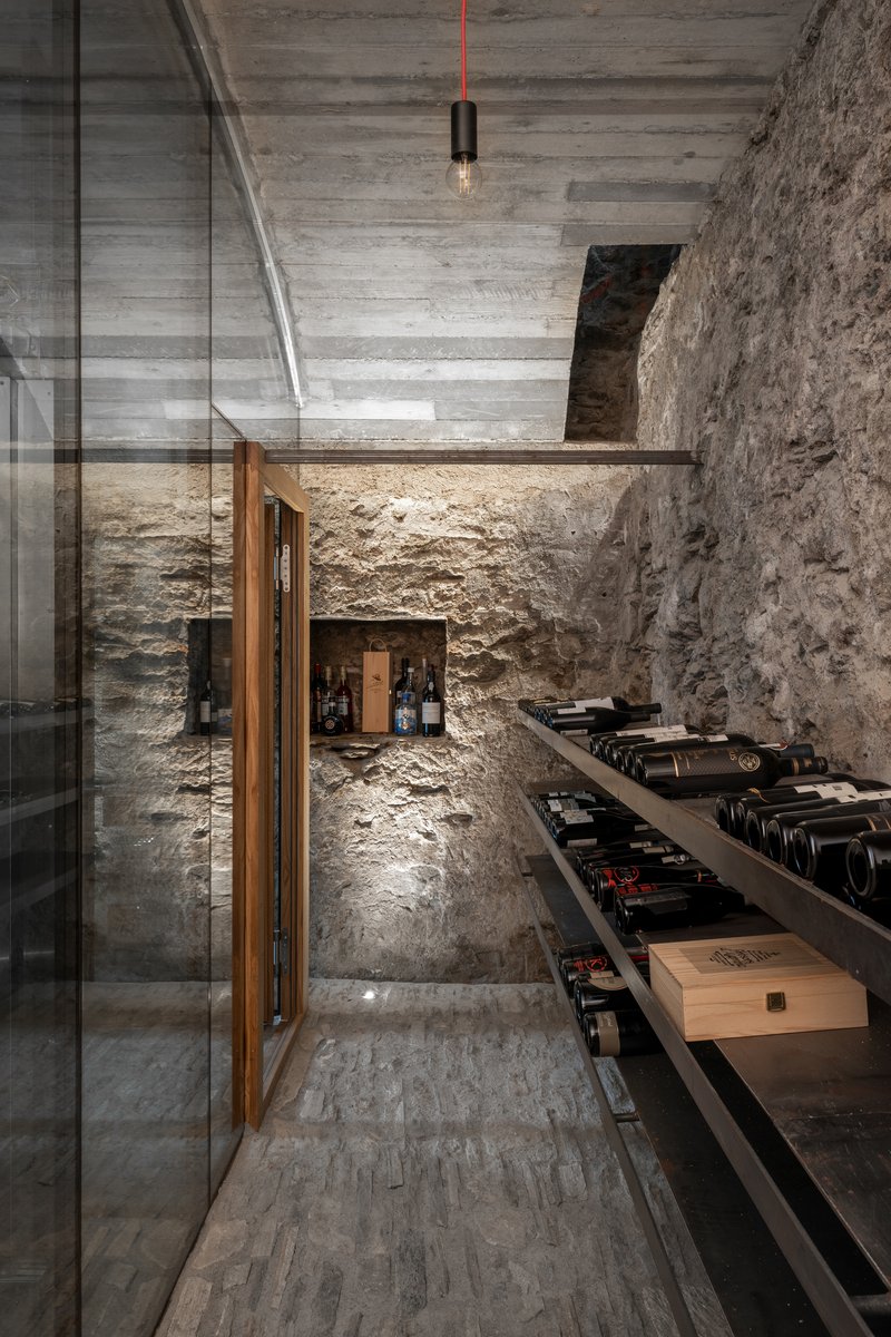 Wine cellar passage with timber-framed glass door and floating shelves under a board-formed concrete ceiling