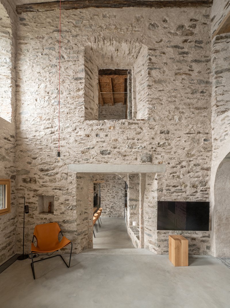Double-height interior space with whitewashed stone walls and suspended mezzanine slab beneath pendant lights