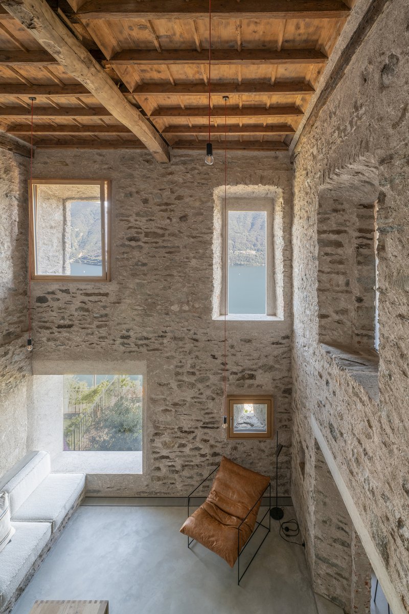 Tall interior room with exposed timber beams and deep-set windows framing mountain lake views