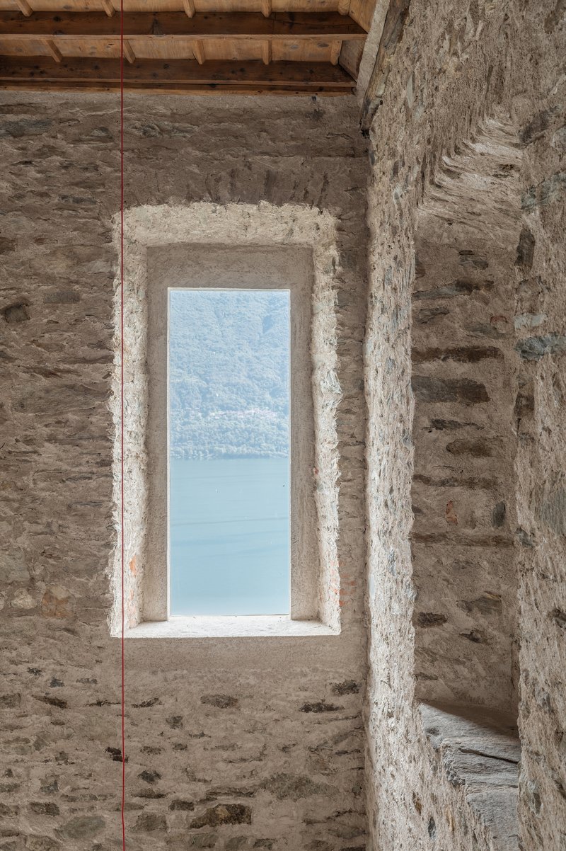 Vertical window cut through thick stone wall revealing a distant lake under open sky