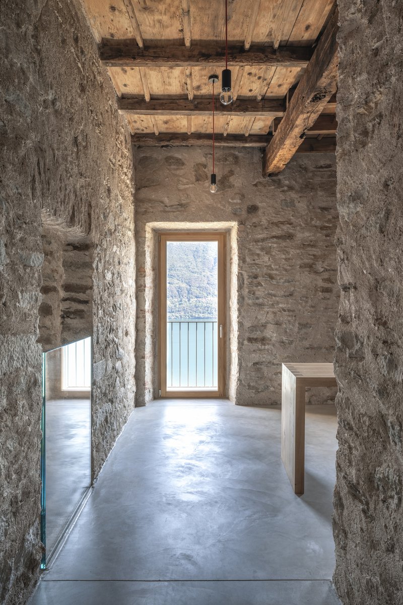 Stone-walled passage with polished concrete floor leading to a timber-framed balcony door