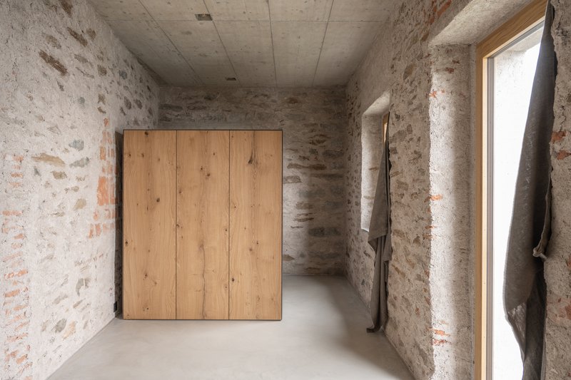 Interior corridor with exposed stone masonry walls, timber wardrobe, and polished concrete floor