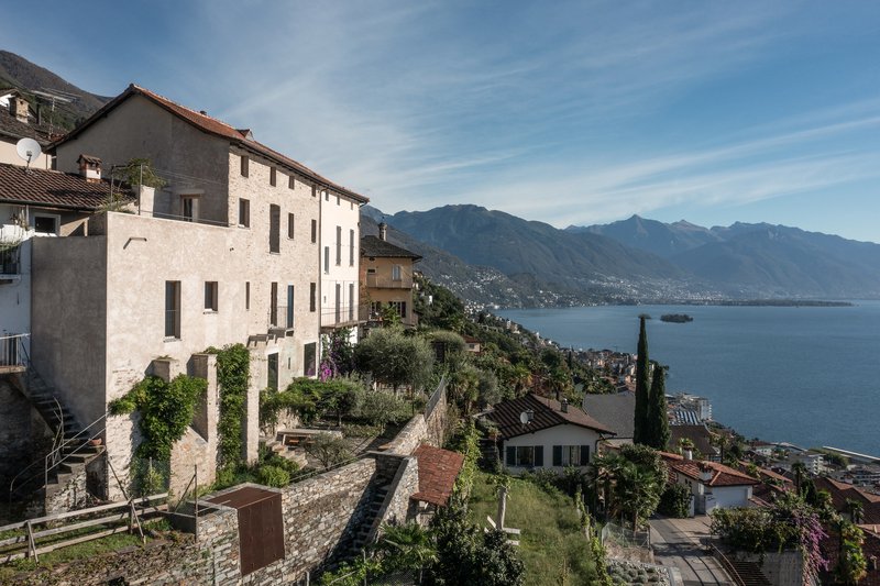 Hillside view of clustered stone houses descending toward a lake with mountains in the distance