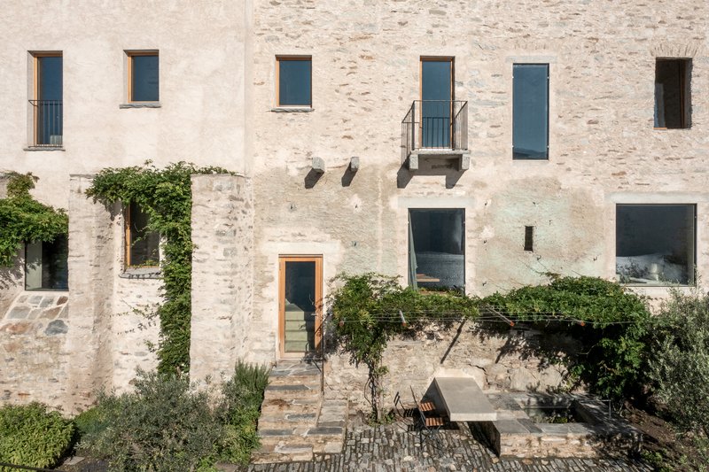 Stone facade with irregular window openings and a small courtyard with climbing vines