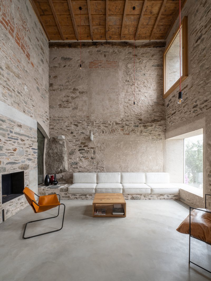 Double-height living space with exposed stone walls, timber beam ceiling, and polished concrete floor