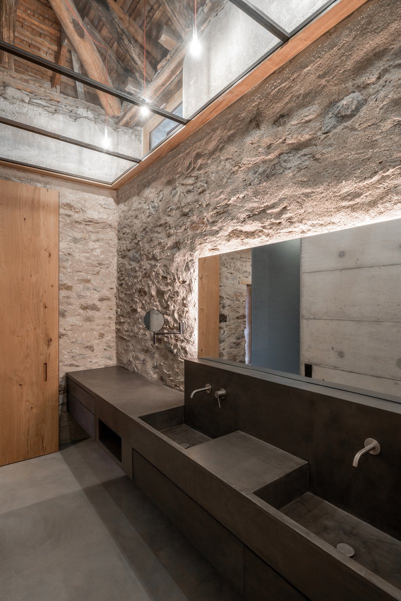 Corner bathroom skylight detail showing timber frame, exposed rafters, and concrete vanity below stone masonry